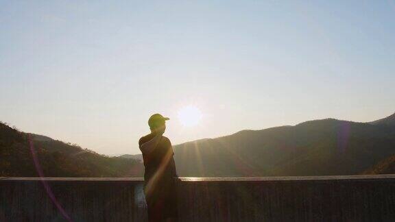 嬉皮士徒步旅行者英俊的男人站在山上用智能手机放松看着美丽的自然看着夕阳的背景