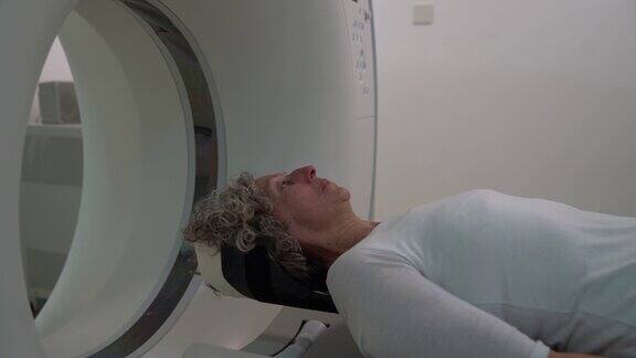 一位年长的妇女躺在平板扫描仪上准备进行脑部核磁共振扫描