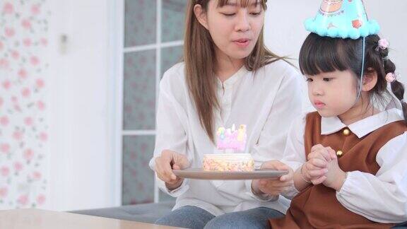 和妈妈在客厅为小女孩的生日聚会亚洲孩子的女孩吹灭生日蛋糕蜡烛亚洲妈妈庆祝女儿的生日