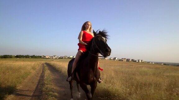 骑马的漂亮姑娘穿着红裙子骑马穿过干燥的草地