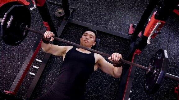 年轻的亚洲肌肉男子躺着和锻炼杠铃卧推在健身房生活方式运动和健美