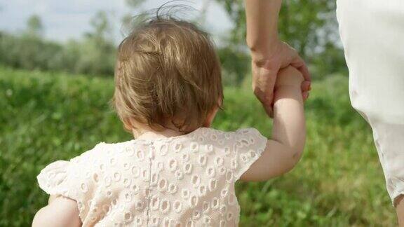 特写慢镜头:小女孩牵着妈妈的手在公园里散步