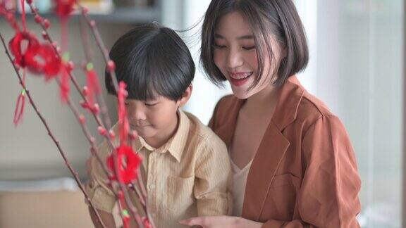 中国新年美丽的女人和她的儿子装饰房子客厅用猫咪柳和装饰准备家庭团聚