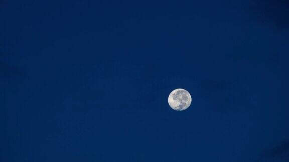 黎明前满月在深蓝色天空中移动的