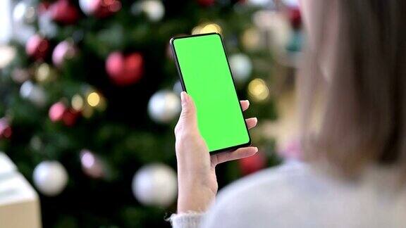 一名女性在圣诞装饰附近使用绿色模拟屏幕智能手机
