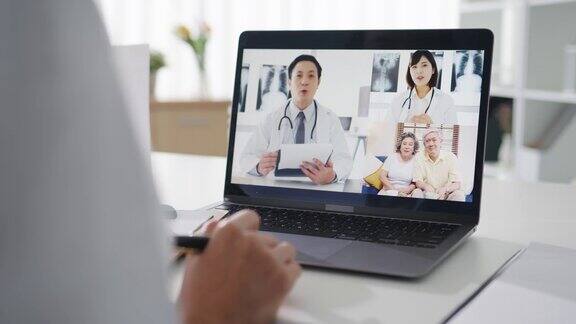 年轻的亚洲女医生在白色医疗制服与听诊器使用电脑笔记本谈话视频电话与病人