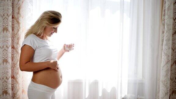 肚子里抱着婴儿的妇女微笑着在房间里拿着一杯纯净水