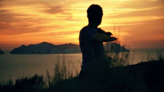 一个人的剪影伸展在山顶上的一个岛屿在日落与大海的背景