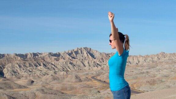 一个兴高采烈的女人站在荒地的山顶上骄傲地举起双臂