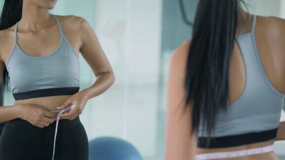 快乐的亚洲女人用测量尺在她的腰看着镜子饮食概念
