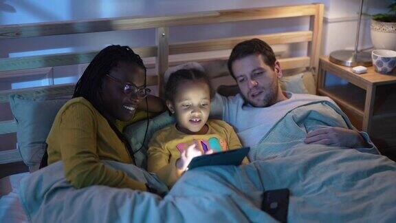 多种族家庭晚上一起在床上使用数码平板电脑