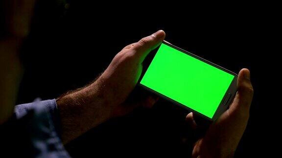 男人用绿色屏幕的智能手机看媒体内容