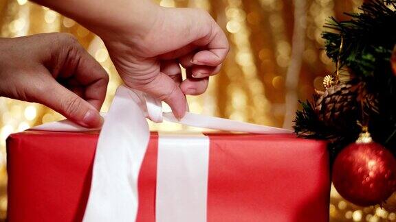 手从礼物盒紧丝带与圣诞灯光背景