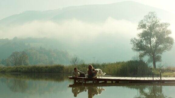 一对年轻夫妇狗和猫坐在湖边的码头上