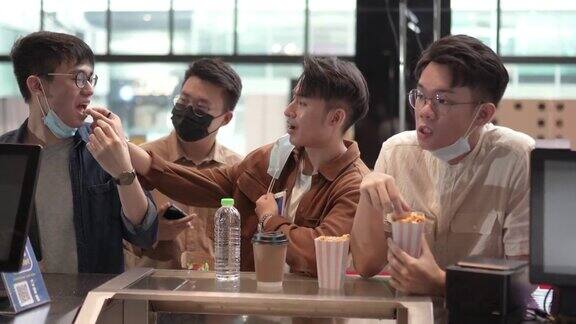 一群亚裔中国朋友一边吃着爆米花一边在电影院前等着看电影