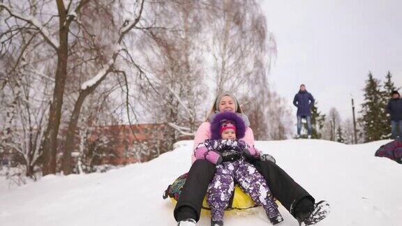 快乐的妈妈和女儿在冬天的雪地里玩雪橇和打雪仗母亲和孩子笑和高兴滑翔在一个充气管圣诞节期间全家游玩公园慢动作