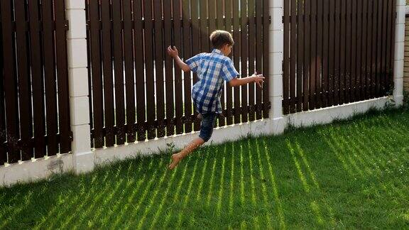 小男孩笑着沿着绿色的院子草坪跑