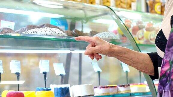 一位老年妇女选择糕点特写指向商店的橱窗