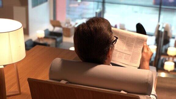 后视图的商务人士放松在机场的贵宾休息室阅读报纸