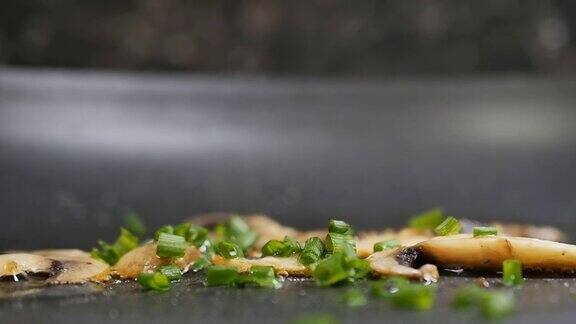 蘑菇在煎锅里用油煎切碎的葱花落在炸蘑菇上慢动作特写摄影