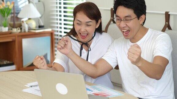 成功的亚洲夫妇夫妇兴奋的好消息从网上笔记本电脑在家里幸福的夫妻高兴与金融投资的好消息
