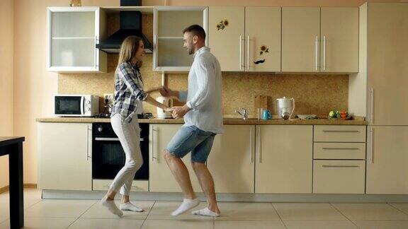 迷人的年轻快乐的夫妇有乐趣跳舞同时在厨房做饭在家里