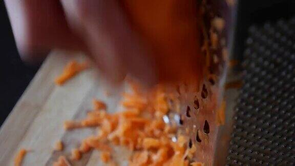 一个女人的手在磨碎器上磨胡萝卜的特写镜头家庭主妇在厨房里磨胡萝卜