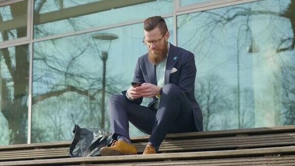 一个商人坐在户外用他的智能手机