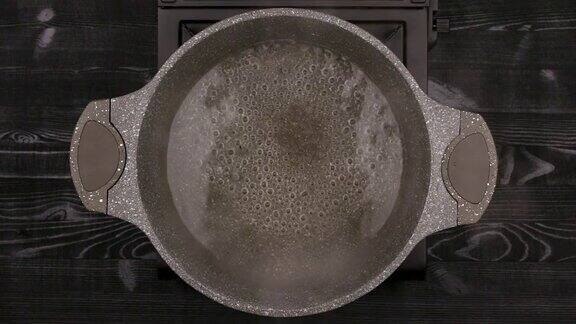 水在带有石头或大理石不粘涂层的金属锅中沸腾平底锅放在煤气炉上背景是一张黑色木桌俯视图