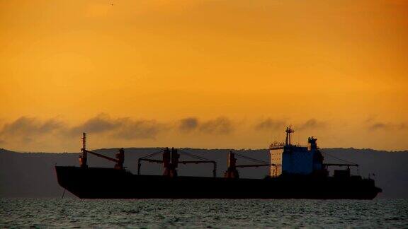 一艘巨大的货船在黄昏的黄光中停泊在海上的一个锚地上