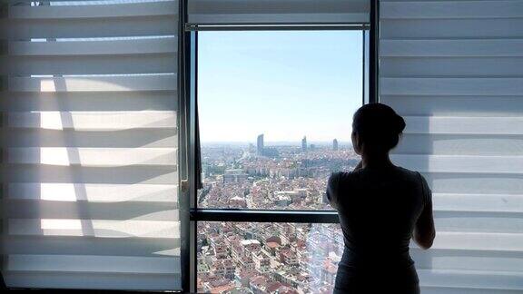 女人打开百叶窗看着窗外的城市全景和伸展
