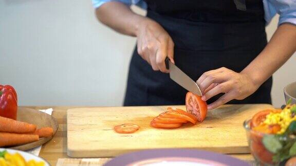 4k镜头镜头近距离拍摄亚洲妇女用刀在厨房的木板上切新鲜的番茄准备和烹饪食物健康和生活方式