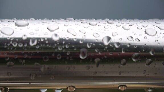 不锈钢扶手上的雨滴映衬着模糊的大海背景特写镜头雨露的水滴聚集在闪闪发光的铬钢杆扶手上