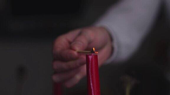 特写镜头男子的手在一间黑暗的房间里用慢镜头点燃了一支红色的节日蜡烛