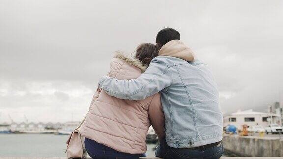 一对年轻夫妇坐在港口的码头上欣赏风景的4k视频片段