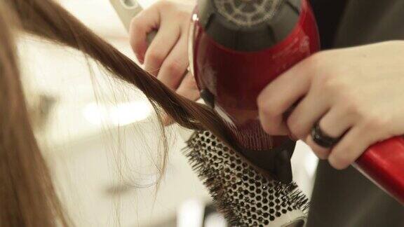 美发师在美发室用吹风机吹干女性头发用梳子定型近距离发型师在美发沙龙做长发造型
