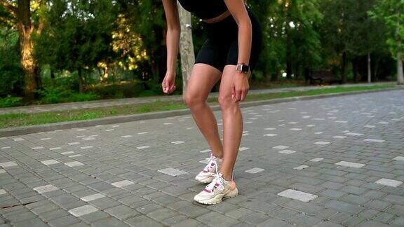 时髦的女性跑步者与发辫在运动穿系鞋带在人行道在夏季绿色公园运动鞋运动鞋