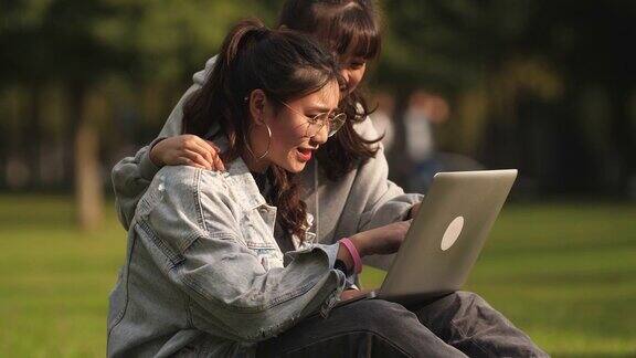 两个亚洲女大学生在校园里用笔记本电脑