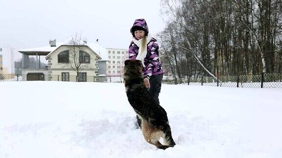 一个穿着冬季夹克的小女孩在雪地里和一只美丽的德国牧羊犬玩耍