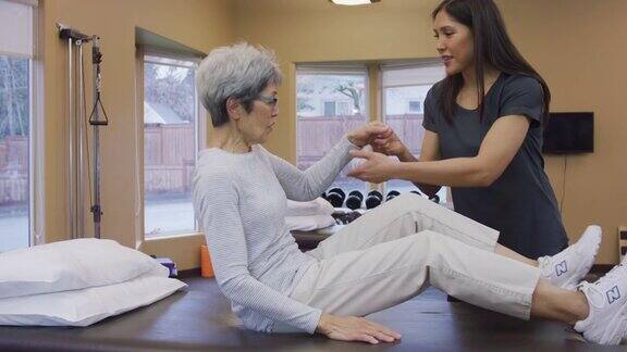 女性物理治疗师帮助一个年长的女性客户离开按摩床