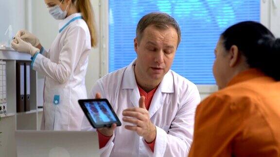 英俊的医生正在向女性病人展示平板电脑上的x光照片