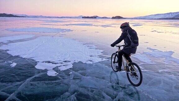 男人在冰上骑自行车骑自行车的人穿着灰色羽绒服背着背包戴着头盔结冰的贝加尔湖的冰自行车的轮胎上覆盖着特殊的尖钉