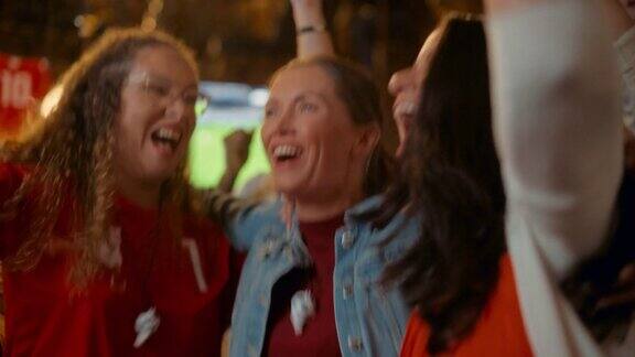 三个女性朋友在体育酒吧看电视直播的足球比赛快乐女孩欢呼呐喊年轻的球迷在球队进球并赢得足球世界杯时庆祝