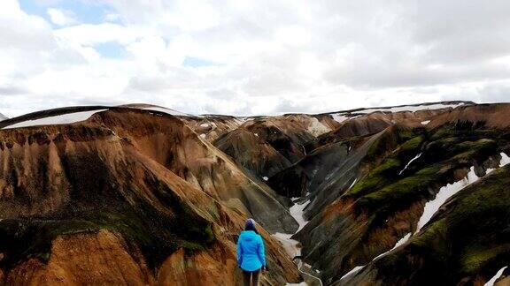 风景鸟瞰图的女人徒步旅行附近的彩色山脉在Landmannalaugar在冰岛