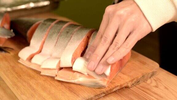 女性手的特写镜头正在木桌上用刀切一条大鲑鱼