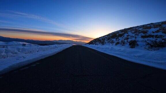 黄昏时分在雪山路上驱车驶向夕阳