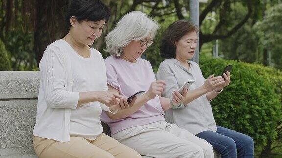 年长的亚洲女性在公园里浏览智能手机