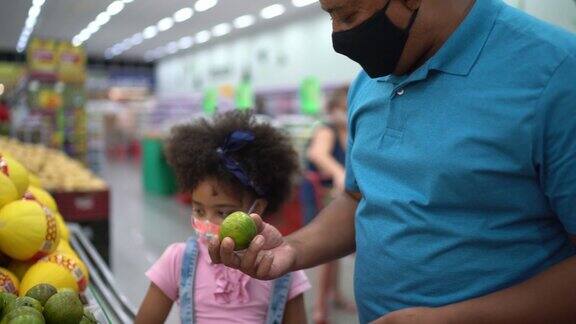 父亲和女儿用智能手机在超市买橘子-戴口罩