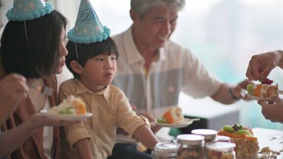亚洲华人多代同堂庆祝生日孙子戴着派对帽在客厅吃生日蛋糕
