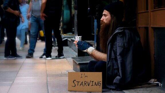 无家可归的人拿着“我饿了”纸板在拥挤的街道上乞讨